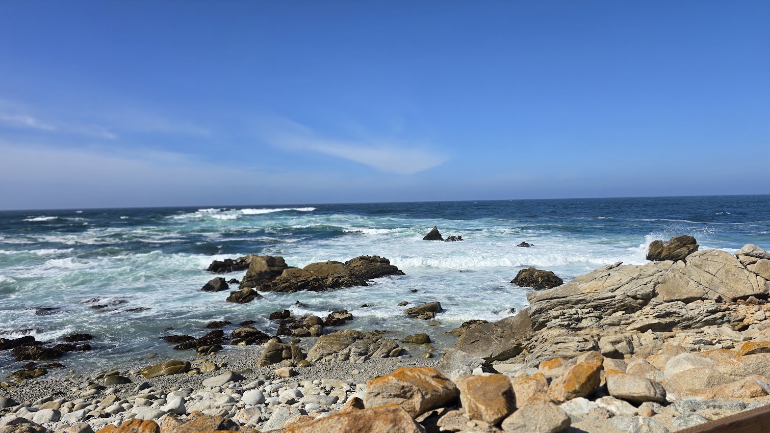 Waves crashing against rocks along the Pebble Beach coastline on a clear blue day